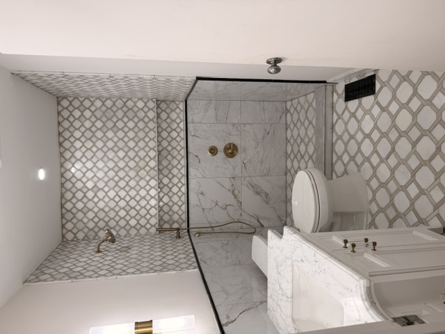 Just-finished bathroom — marble lattice-tile walk-in shower, brass fixtures, marble-top vanity